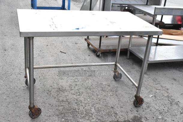 Stainless steel table with commercial casters. Shows signs of use, sturdy with rust on wheels. Ideal for industrial use.