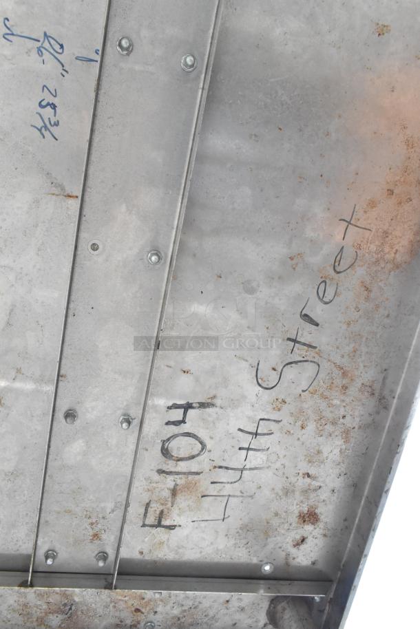 Stainless steel table underside with rust and markings. Equipped with commercial casters for mobility. Good condition.