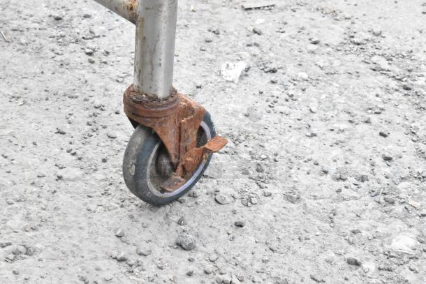 Stainless steel table on commercial casters, showing a close-up of a worn, rusted wheel indicating usage and wear.