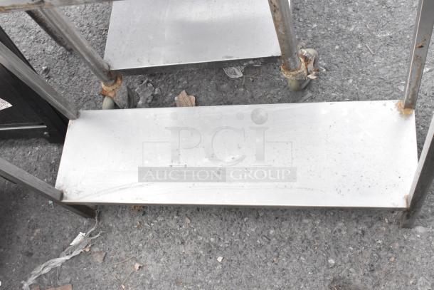 Stainless steel table with under shelf, visible wear and rust on wheels, sturdy construction, ideal for industrial use.