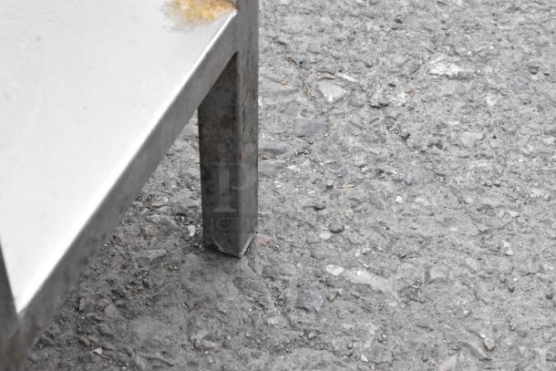 Stainless steel table leg with slight corrosion at the top corner, standing on a rough concrete surface.