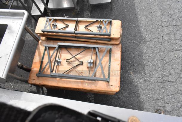 16 wooden folding tables, stacked, metal legs folded. Used condition. Auction lot multiplier: 16 times your bid.