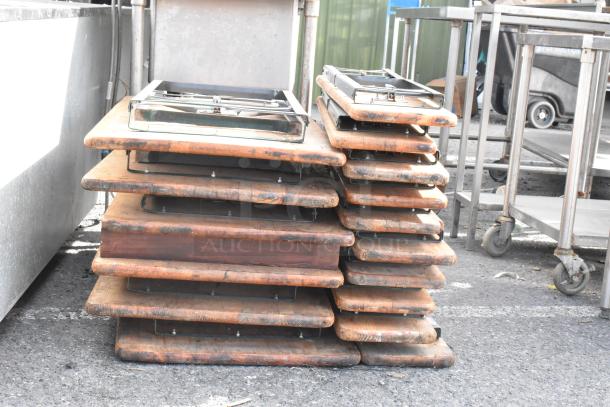 16 wooden folding tables, stacked. Each shows wear and scuff marks, metal frames visible. Auction lot item, 16 times your bid.