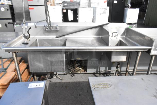 Stainless steel 2 bay sink with 2 faucets, commercial use, used condition, visible plumbing parts underneath.