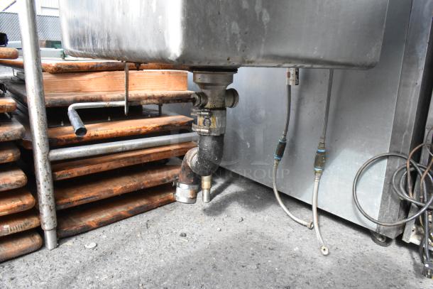 Stainless steel 2 bay sink with 2 faucets, visible piping and connectors, showing signs of wear.