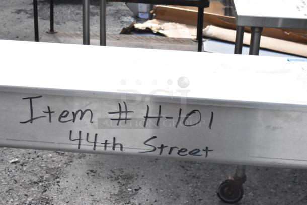 Stainless steel table with backsplash, in used condition. Marked "Item # H-101, 44th Street." Equipped with wheels.