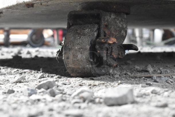 Rusty caster wheel of a commercial undercounter cooler on rough ground.