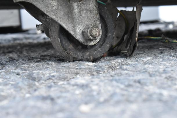 Commercial caster wheel of stainless steel undercounter cooler, showing dirt and wear, indicating frequent usage.