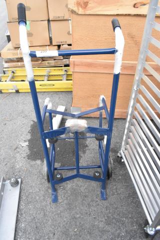 Blue metal barrel dolly, brand new with minor scratches and dents, features black handles and rubber wheels.