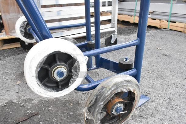 Brand new blue metal barrel dolly with visible scratch and dent. Features rubber wheels with protective plastic wrap.