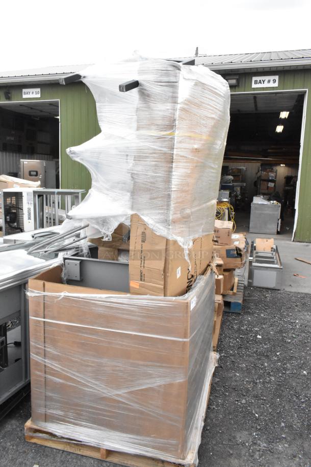 Pallet of 8 new scratch and dent items, including Regency stainless steel work table and pass-through shelf, wrapped in plastic.