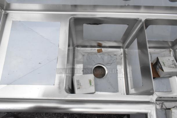 Regency 600S3141414C stainless steel 3-bay L-shaped sink with dual drain boards; no legs, new but with scratches.