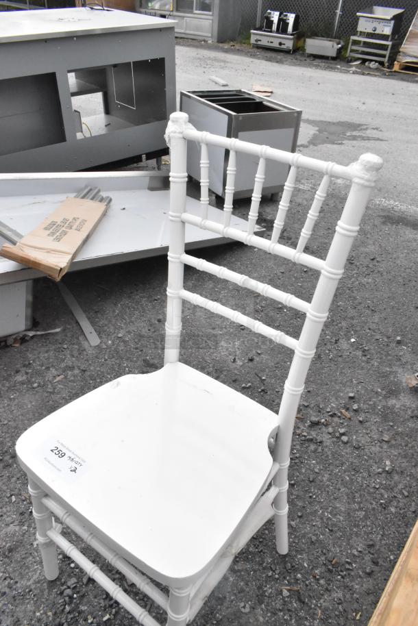 White Chiavari stackable banquet chair with scratches, visible wear. Auction tag showing "259". Weathered outdoor background.
