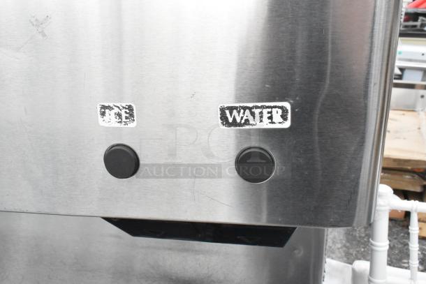 Hoshizaki DCM-500BAH stainless steel ice maker and dispenser, labeled "ICE" and "WATER" with buttons, on SD-500 stand.