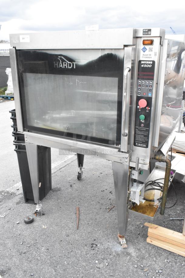 Hardt Inferno 4500 stainless steel commercial rotisserie oven, natural gas powered, with skewers and metal legs on casters.