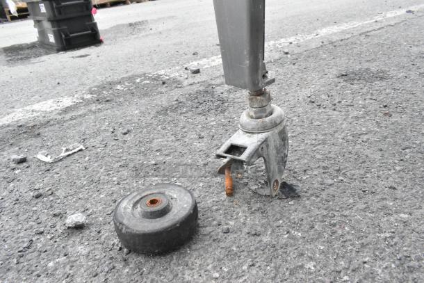 Hardt Inferno 4500 rotisserie oven caster, missing wheel, on asphalt surface; shows part of metal leg and loose wheel.