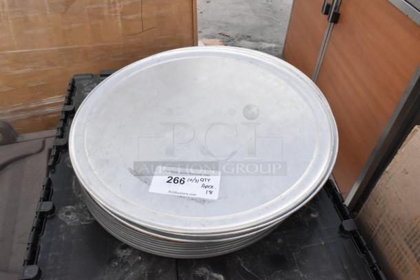 18 brand new metal round baking pans, scratch and dent condition, stacked, label shows auction lot details.
