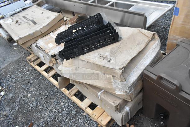 Four brand new scratch and dent items on a pallet, including 600TSB3072S stainless steel work table, 460EB3036 black epoxy wire shelf, and 164TB3030 cast iron table base plate. Boxes show wear.