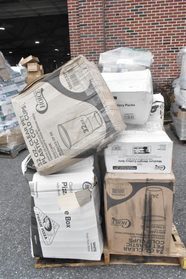 Boxes of scratch and dent items including 32 oz plastic cups, cutlery packs, and pizza boxes stacked on a pallet.