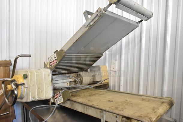 Rondo Seewer metal commercial reversible dough sheeter, no legs, used condition, safety labels visible, industrial setting.