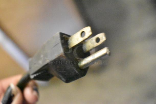 Close-up of a three-prong plug for an espresso bean grinder, indicating 115 volts and 1 phase power requirement.
