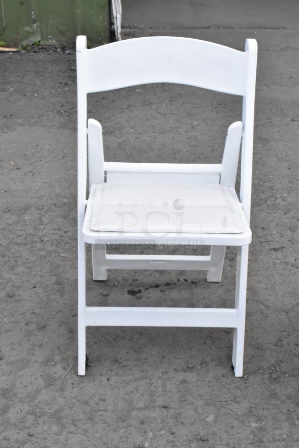 White folding banquet chair on concrete surface, sturdy design, padded seat, offered in bulk (90 items) for auction.