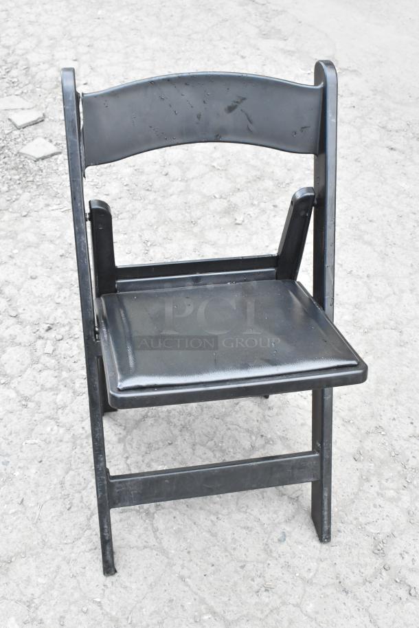 Black folding banquet chair on textured ground, showing minor wear. Part of a lot of 90 items for auction.