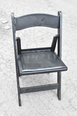Black folding banquet chair on textured ground, showing minor wear. Part of a lot of 90 items for auction.