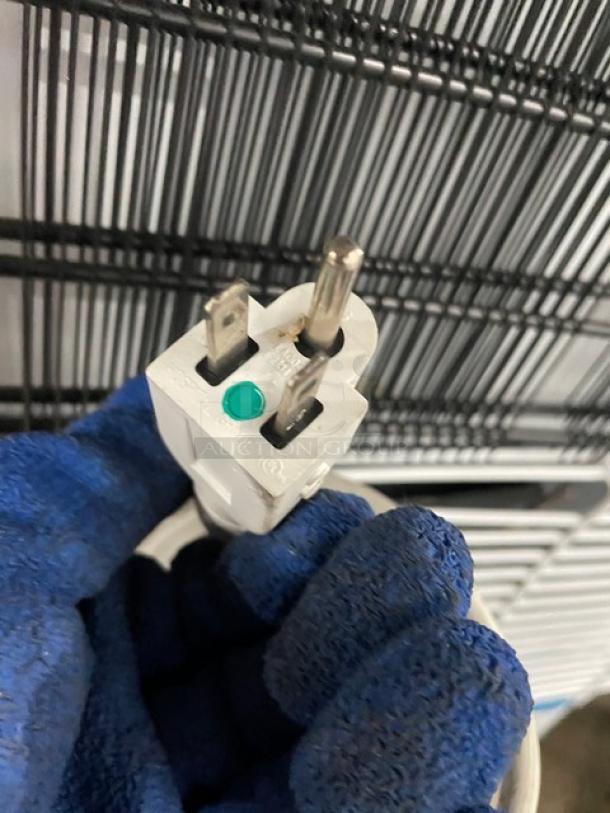 Close-up of a power plug for an Accucold ARS6PV refrigerator, showing prongs and protective gloves holding it.