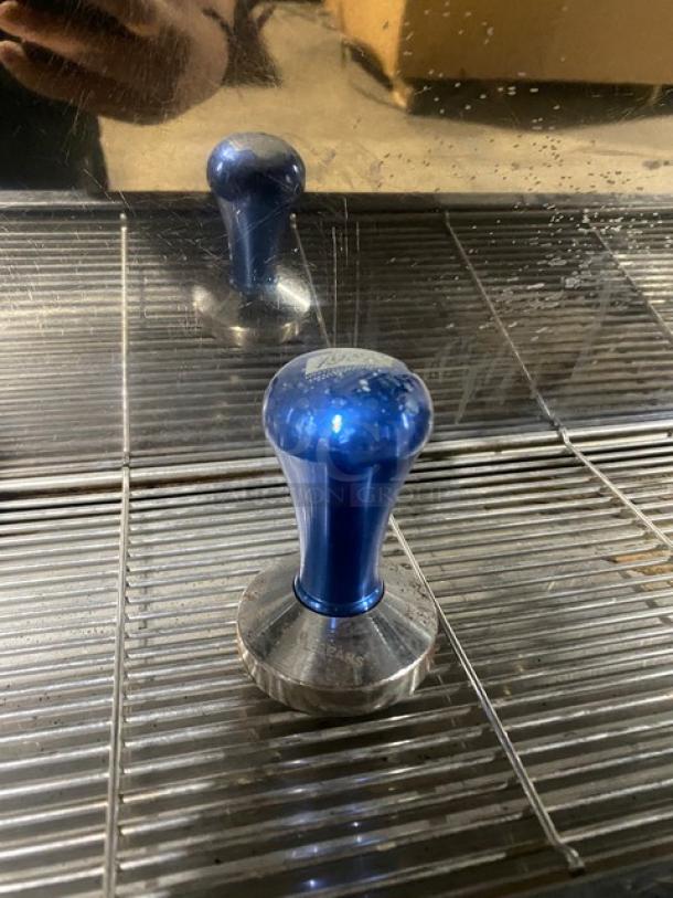 Blue espresso tamper on a stainless steel drip tray, part of a Conti CC103DTC 3-group automatic espresso machine.