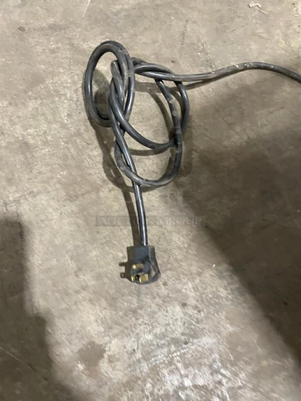 Coiled power cord on concrete floor, suitable for connecting industrial appliances.