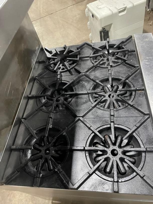 Garland commercial stainless steel 6 burner range/oven with backsplash, overhead salamander shelf, and wired oven rack on casters.