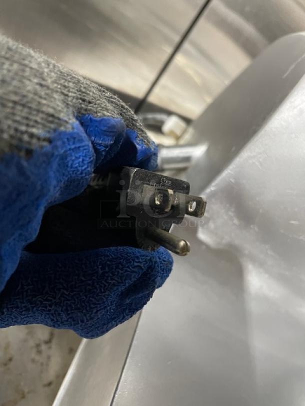 Avantco commercial deli meat slicer plug, showing a standard three-prong design. Gloved hand holding the plug.