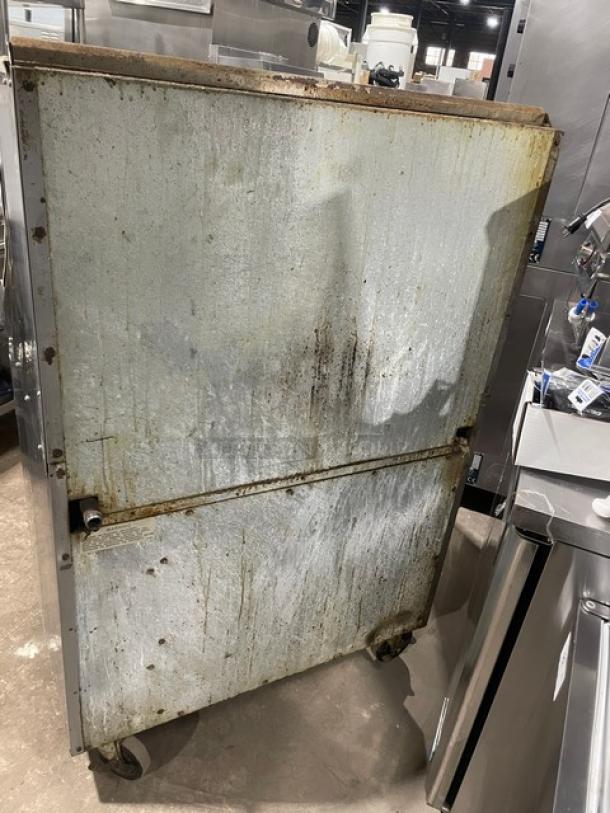 Rear view of Imperial stainless steel 6-burner range/oven combo on casters, showing wear and rust. Equipped with splash backs and overhead salamander shelf.