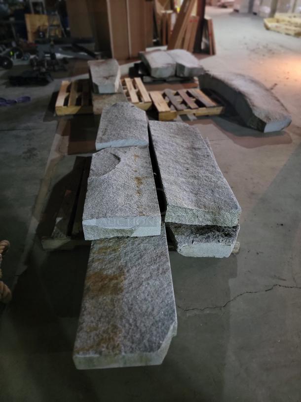 Rustic grey granite slabs on pallets, assorted lengths. Natural texture, ideal for landscaping projects like steps and benches.