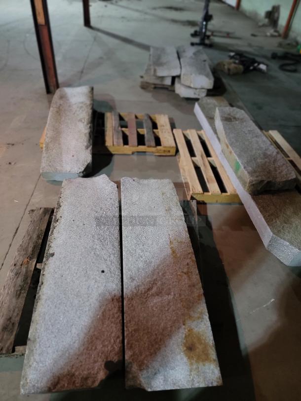 Rustic grey granite slabs with natural texture on pallets, suitable for landscaping and construction projects. Assorted lengths.