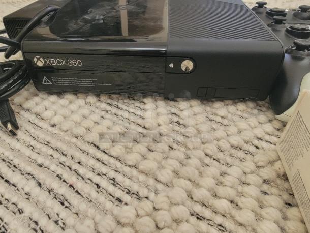 Xbox 360 S console on textured surface, power cable attached. Unit features glossy and matte finishes, in good condition.
