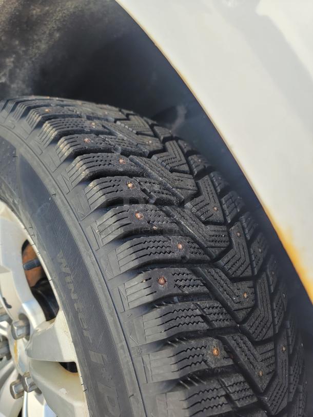 Close-up of a studded winter tire on a 2015 Chevy Equinox SUV. Tire tread and sidewall "Winter R" markings visible.