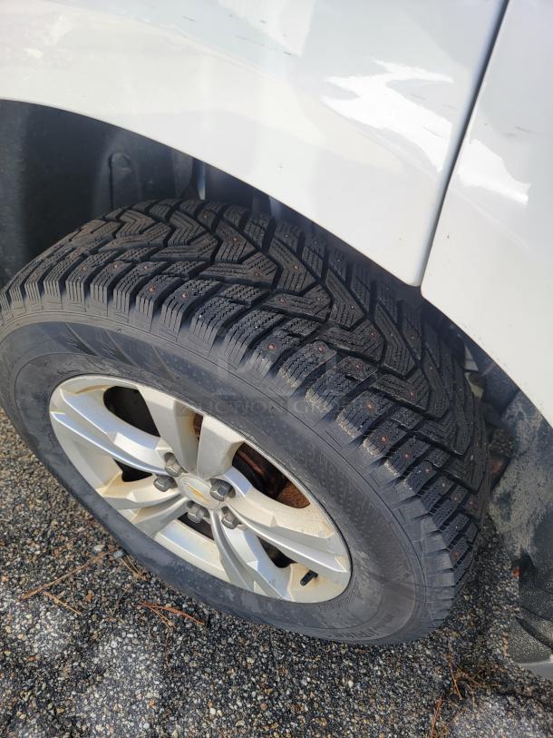 Front tire and alloy rim of a 2015 Chevy Equinox, showing good tread condition on a gravel surface.