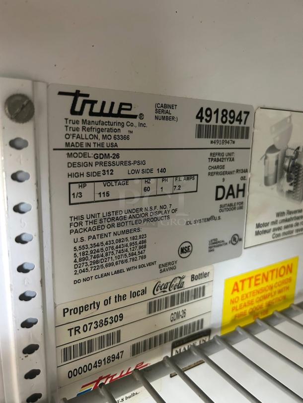 Label on True GDM-26-HC~TSL01 glass door merchandiser showing model, voltage, refrigerant type, serial number, and NSF certification.