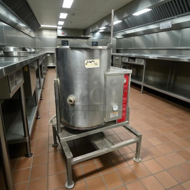 Industrial steel kettle on a stand in a commercial kitchen. Features control panel and spout. Label reads "DWIN 12".