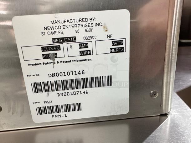 Stainless steel Newco FPM-1 cold beverage dispenser with label showing model, serial number, and manufacturing details.