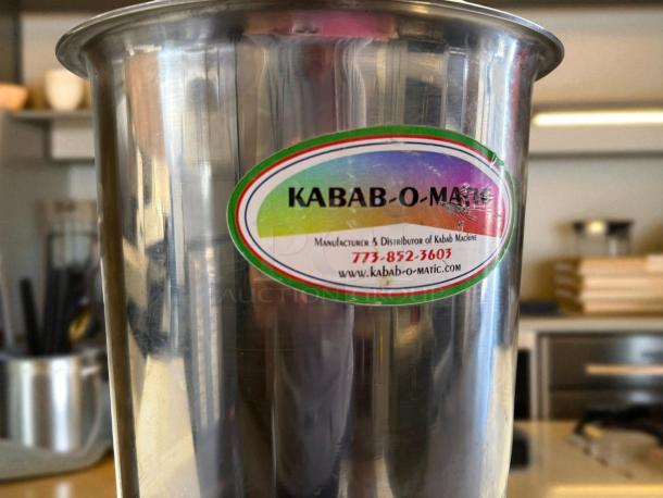 Heavy-duty stainless steel Kabab-O-Matic kebab maker in excellent condition with label showing contact details and website.