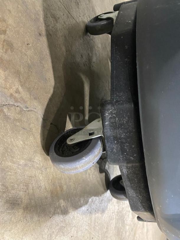 Rubbermaid BRUTE Series 44 Gal. gray trash container with dolly, scratches visible, sturdy wheels for mobility.