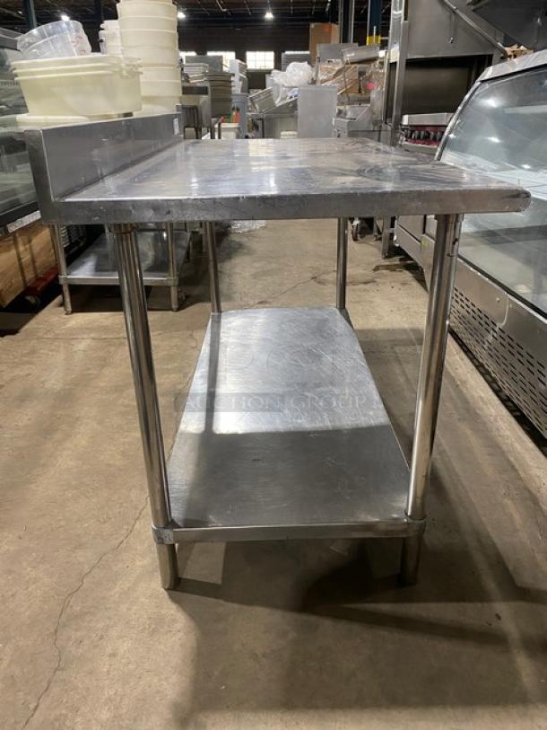 Commercial stainless steel worktop table with single undershelf, upturned backsplash, and four legs. Industrial-grade condition.