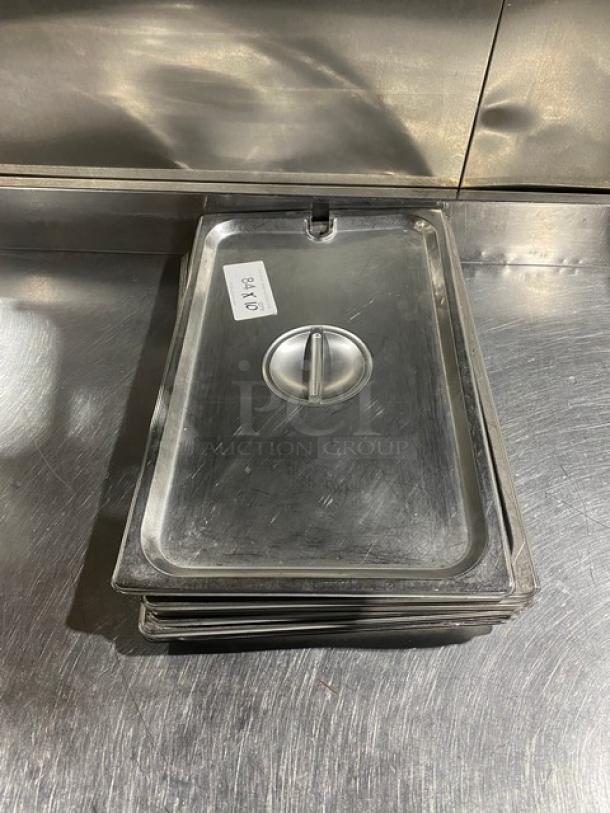 Commercial stainless steel notched hotel pan lid, stack of lids on metal surface, visible label with bid info.