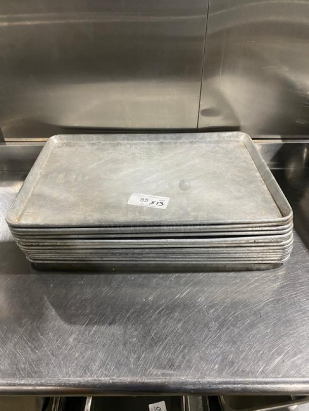 Stack of commercial baking sheet pans, slightly worn, each labeled "85 X 13." Used condition, suitable for high-volume baking.