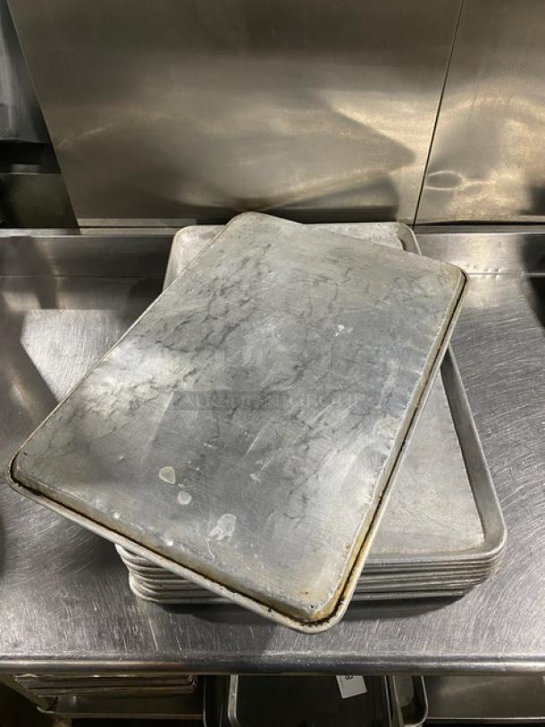 Stack of commercial baking sheet pans, used condition, metal surface with wear marks, auction for 13 pans.