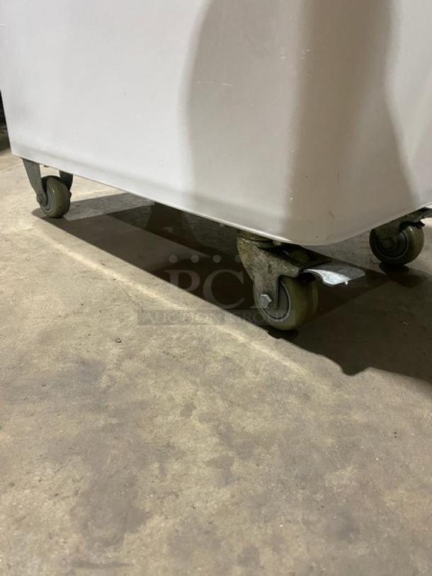 Winco commercial white portable food storage bin with clear lid, on casters, showing robust wheels, in good condition.