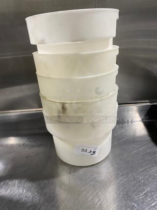 Stack of commercial white round food storage containers with handles, slightly worn, on a metal surface. Label reads "94 +5."
